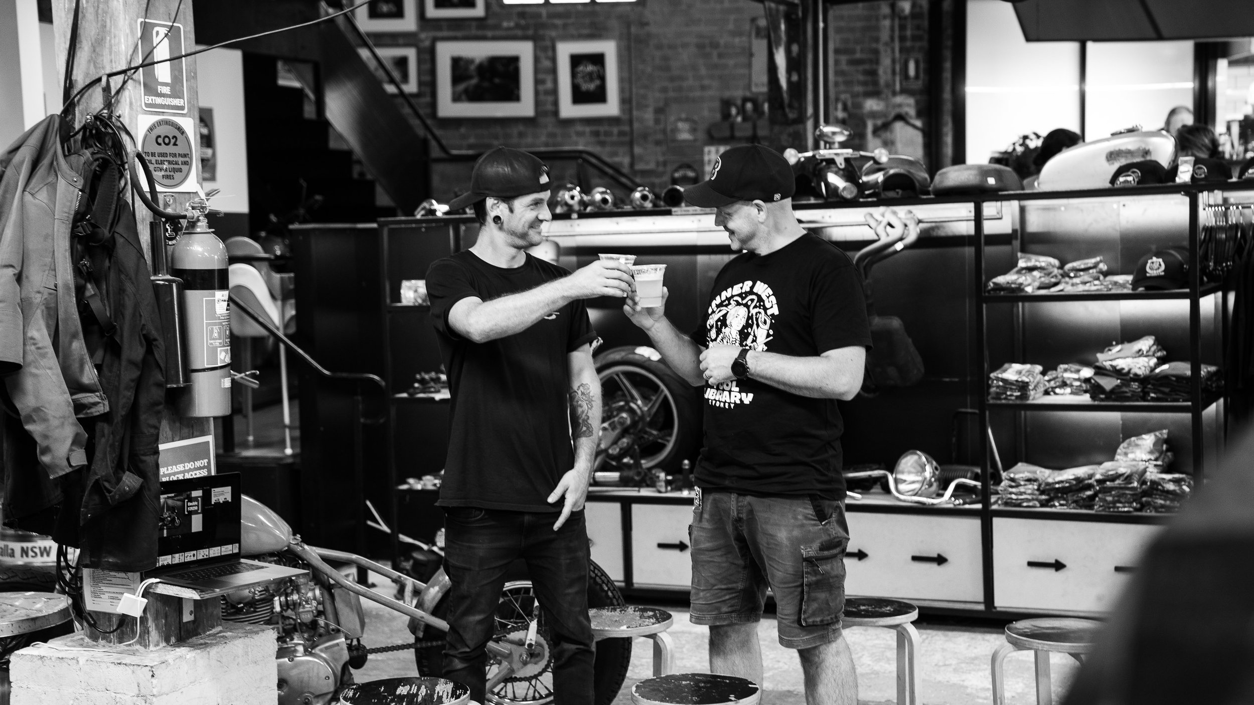 Two guests cheering with beer in hand amongst motorbike merchandise at Young Henrys