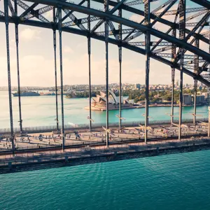 a side view of the Sydney Harbour Bridge with runners and the Sydney Opera House in the background