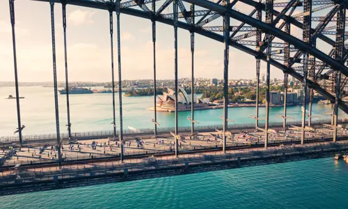 a side view of the Sydney Harbour Bridge with runners and the Sydney Opera House in the background