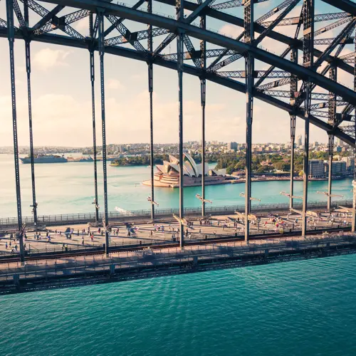 a side view of the Sydney Harbour Bridge with runners and the Sydney Opera House in the background