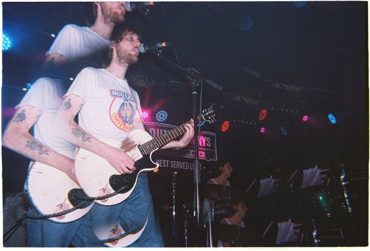 Musician playing guitar with band on stage at Young Henrys