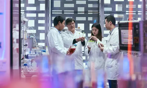 Four People In A Laboratory Setting Engaging In Discussion Surrounded By Scientific Instruments Indicating A Professional Research Environment