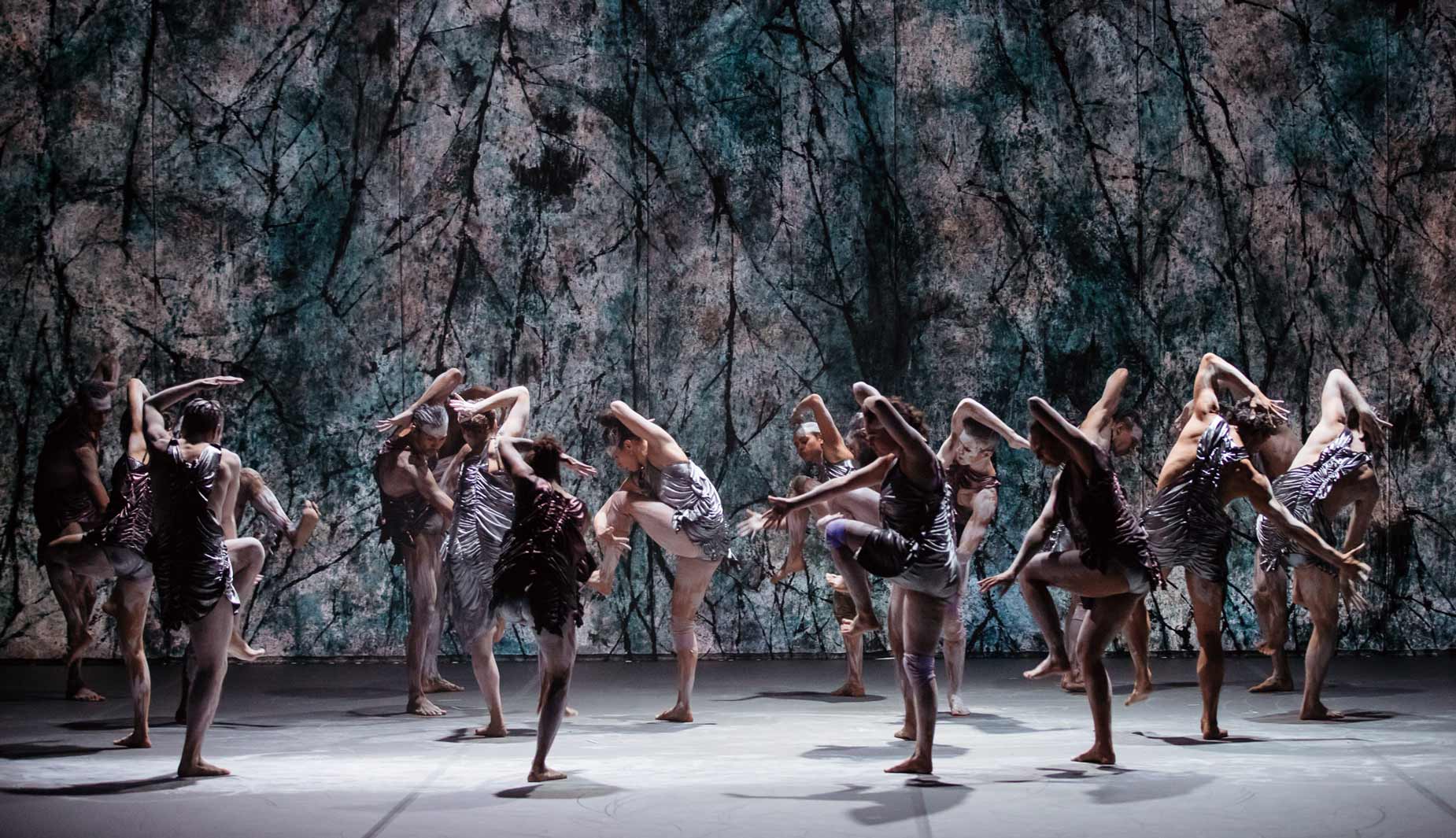Aboriginal and Torres Strait Islander dancers from Bangarra Dance Theatre performing a contemporary piece on stage against a large textured backdrop