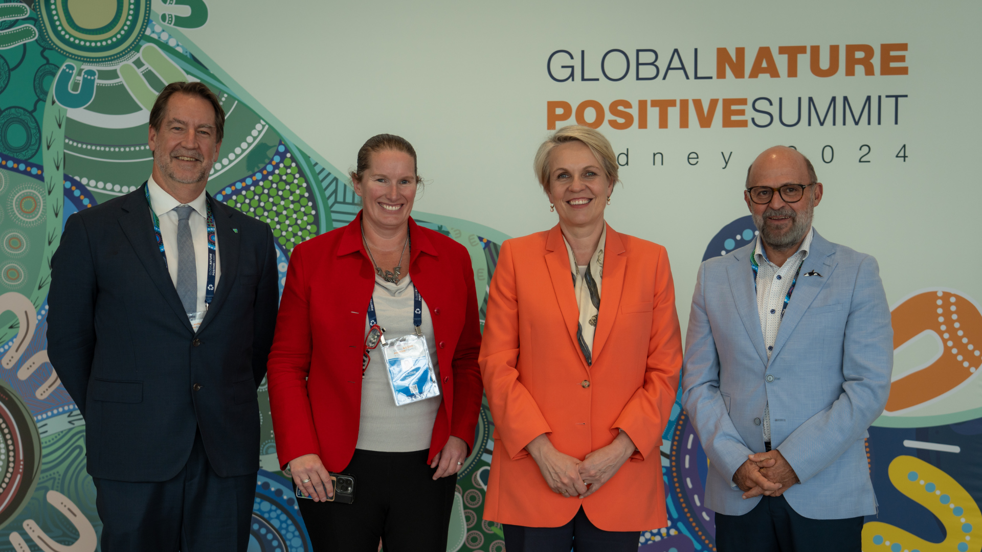 Four Conference Attendees Standing In Front Of Large Entrance Board With The Title Name Of Conference Global Nature Positive Summit Logo