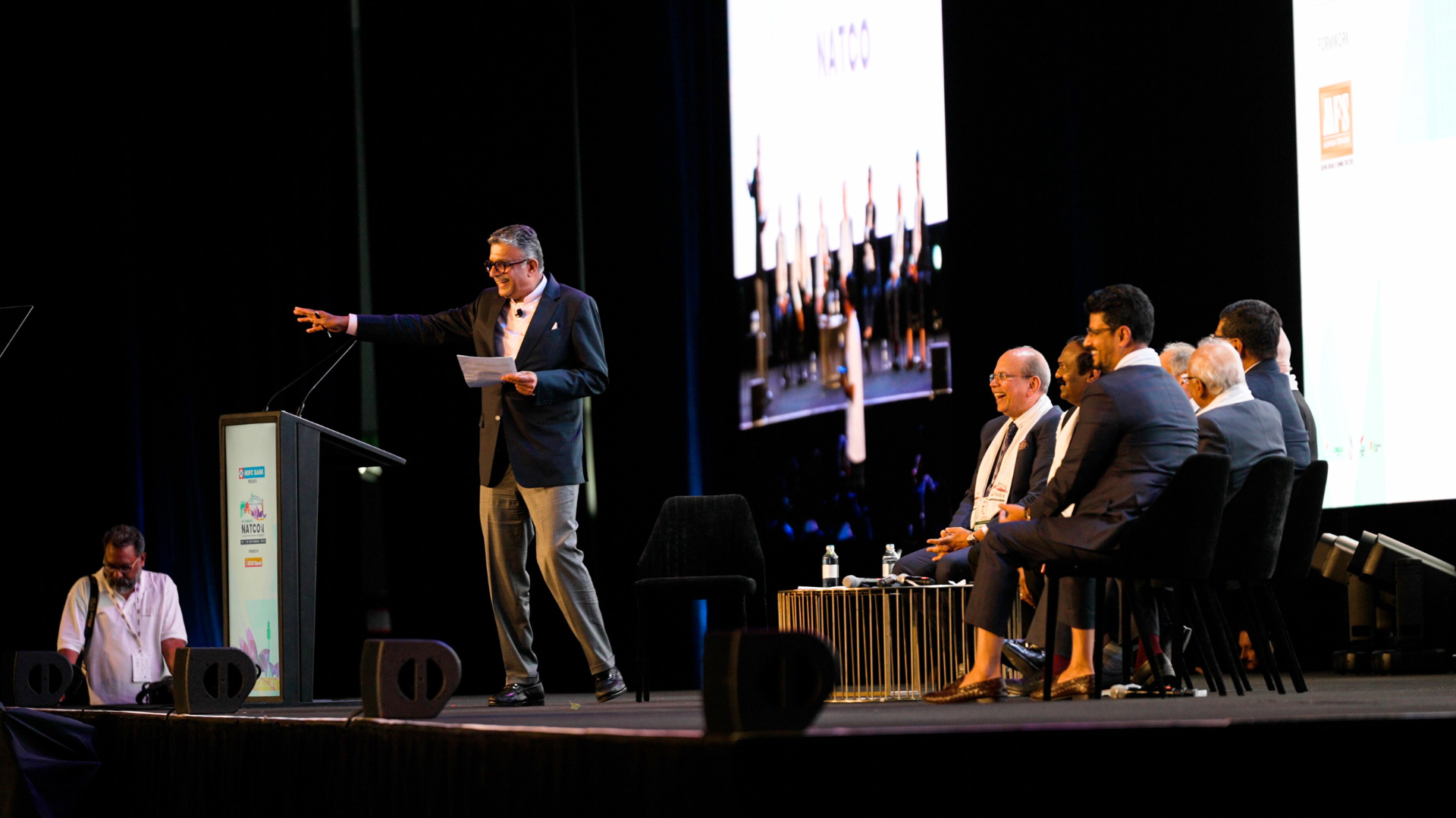 Panel of speakers on stage, smiling and looking at the delegate crowd