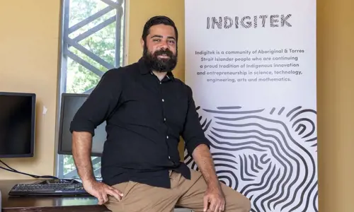 Liam Ridgeway, Co-Founder at Indigitek, posing in front of an Indigitek banner