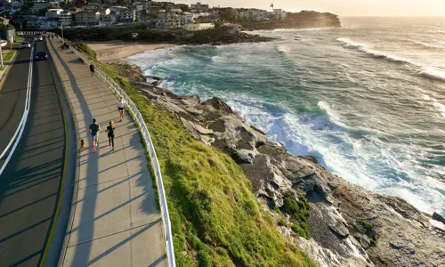 People jogging and walking along a cliffside coastal walkway overlooking the ocean