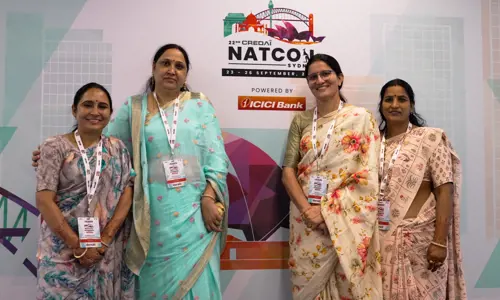 Group of four women delegates in traditional sari outfits, standing in front of the Credai Natcon signage board at entrance
